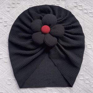 Detail of black ribbed turban hat for babies featuring a large flower with a red button