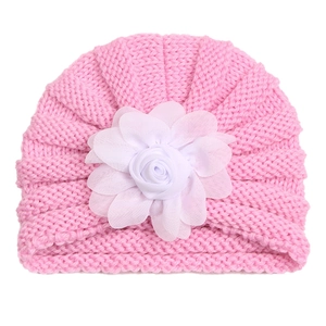 Détail d'un bonnet tricoté rose pour bébé avec une grande fleur décorative blanche