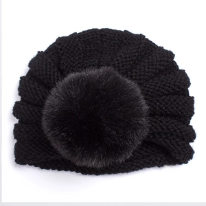Gros plan détaillé d'un bonnet turban tricoté noir pour bébé avec un grand pompon en fourrure