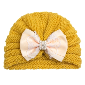 Detail of yellow knit baby hat featuring a lace bow with decorative pearls