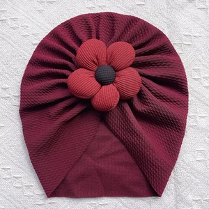 Detail of burgundy waffle knit baby turban hat featuring a large red fabric flower