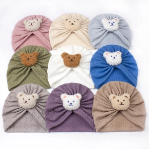 Nine colorful baby knit turban hats with cute plush bear patches on a white background
