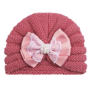 Detail of pink knit baby hat with satin bow lace edges and white pearl beads