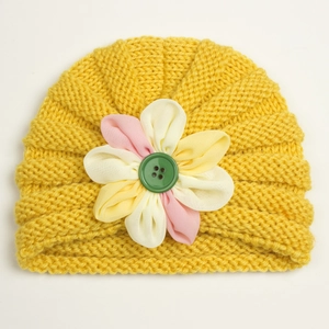 Detailed close-up of warm yellow knit baby beanie with button and floral patch