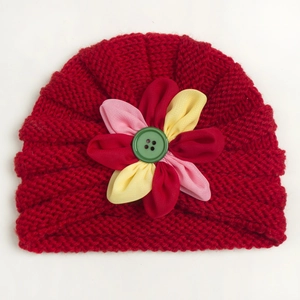 Detail of red knit baby beanie featuring a colorful fabric flower and green button accent
