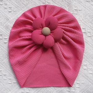 Detailed shot of pink textured baby turban hat with a large 3D flower and button center