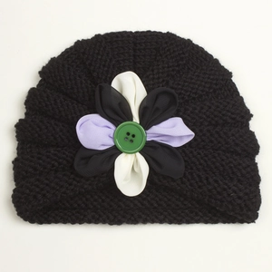 Detailed close-up of a black knit baby turban with a floral patch and a green button
