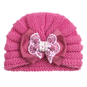 Close-up of rose pink baby knit beanie with large pearl bow and lace detail on white background