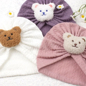 Detail of knitted baby beanies in pink, white and purple with cute plush bear patch