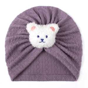 Detail of purple knitted baby turban with white plush bear and textured cable patterns