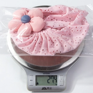 Dettaglio del cappello rosa per neonati con fiore su una bilancia che pesa 27,4g