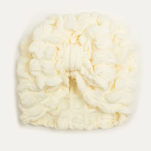 Detail of cream white baby turban hat featuring waffle texture and a large bow