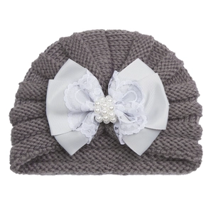 Detailed knit texture of grey baby winter hat with large white pearl bow and lace accent