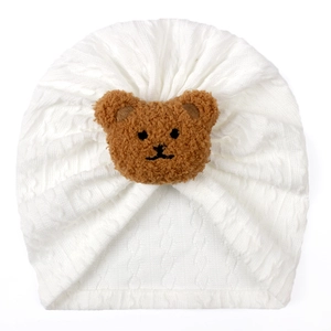 Close-up of white baby beanie featuring cable knit texture and a cute plush bear patch