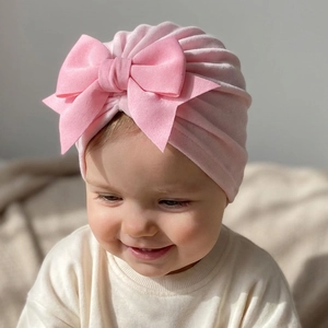 Détail d'un bonnet turban rose pour bébé avec un grand nœud décoratif et maille côtelée souple