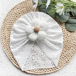 Dettaglio del turbante bianco per neonati con ricamo a traforo e grande fiore decorativo