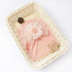 Detail view of pink baby turban hat with sequined mesh flower in a decorative basket