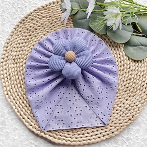 Dettaglio del turbante lilla per neonati con fiore 3D su un tappetino di paglia