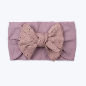 Détail d'un bandeau bébé avec grand nœud en dentelle et broderie sur tissu en tricot rose