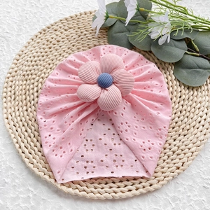 Dettaglio del cappello rosa traforato per neonati con grande fiore 3D su un tappetino di paglia