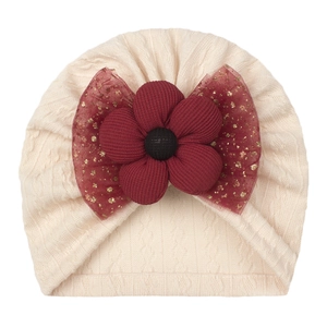 Detail of beige baby knit hat featuring a burgundy fabric flower and gold glitter mesh bow