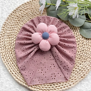 Dettaglio del cappello in maglia traforata per neonati con grande fiore su tappeto in paglia