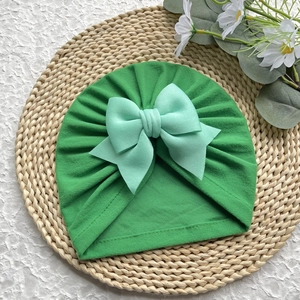 Détail du turban pour bébé vert émeraude avec un grand nœud sur un tapis tressé