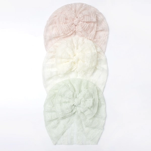 Dettaglio di tre turbanti in pizzo per neonati in rosa, beige e verde con fiocchi