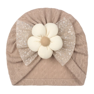 Detail of baby knit hat with khaki cable texture, white flower and sequin mesh bow