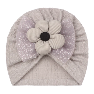 Detail of baby beanie with beige flower and purple sequin bow on grey knit fabric