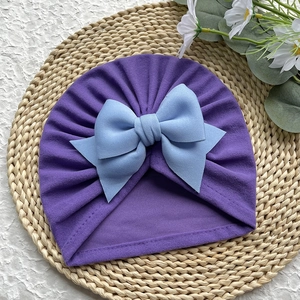 Détail du bonnet turban pour bébé en tricot violet foncé avec un grand nœud bleu clair