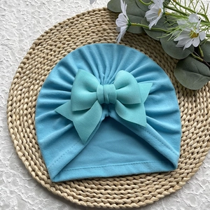 Détail d'un bonnet turban pour bébé avec un grand nœud souple et une texture plissée bleu clair