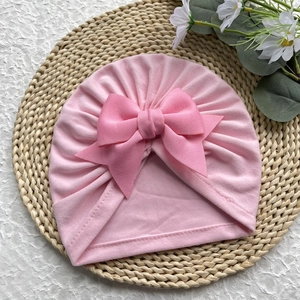 Gros plan d'un bonnet turban rose pour bébé avec un grand nœud sur un tapis tressé