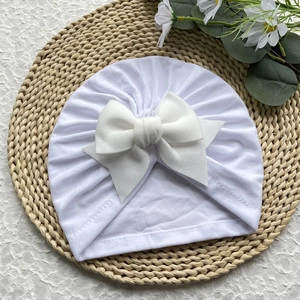 Détail d'un bonnet turban blanc pour bébé avec un grand nœud et des plis doux