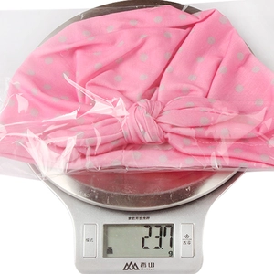 Bonnet bébé rose à pois avec nœud oreilles de lapin sur une balance montrant le poids léger