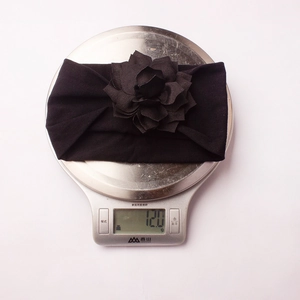Detailed view of black fabric floral baby headband being weighed at 12.0g on a scale