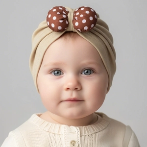 Close-up of baby beige knit hat featuring a brown polka dot bow detail for infants