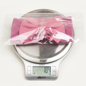 Pink bow baby headband weighing 18.4g on a digital scale to show lightweight material