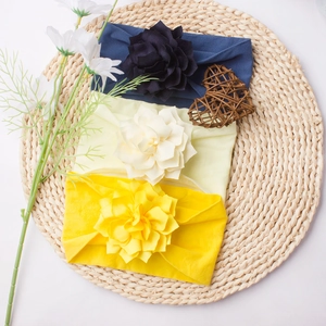 Three-piece set of soft elastic baby headbands with large fabric flowers on a woven mat