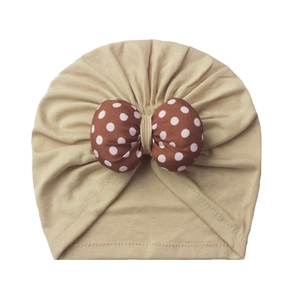 Detailed view of baby turban hat featuring a large brown polka dot bow on khaki fabric