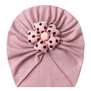 Pink knit baby hat featuring a large polka dot flower decoration and plush center ball