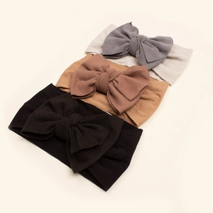 Detail of three soft nylon baby headbands with large bows in grey, brown, and black
