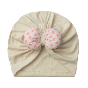 Close-up of soft beige knit baby turban hat featuring a pink polka dot bow decoration
