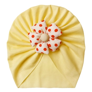 Detail of baby turban hat in light yellow with a red polka dot white flower accent