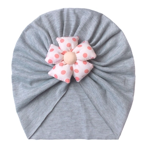 Detail of grey baby turban hat featuring a soft pink polka dot floral ornament on white background