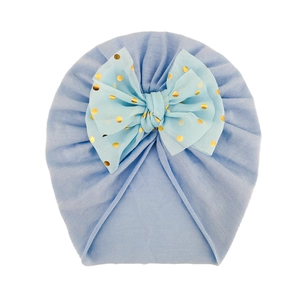 Cappellino neonato azzurro con grande fiocco a pois dorati su morbido tessuto a maglia