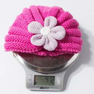 Close-up showing the weight of a rose red knitted baby turban hat with purple flower