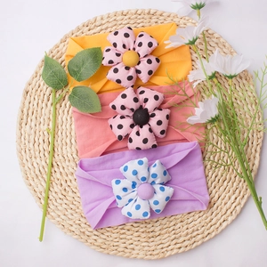 Three-piece set of stretchy baby headbands with large polka dot flowers on woven mat