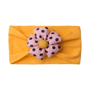 Detail of baby headband featuring large pink polka dot flower on yellow elastic band