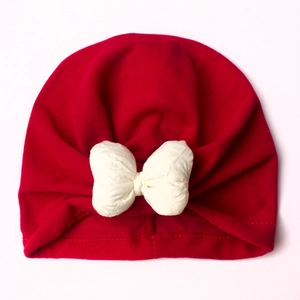 Detail of red baby turban hat with a large white bow on soft ribbed cotton fabric